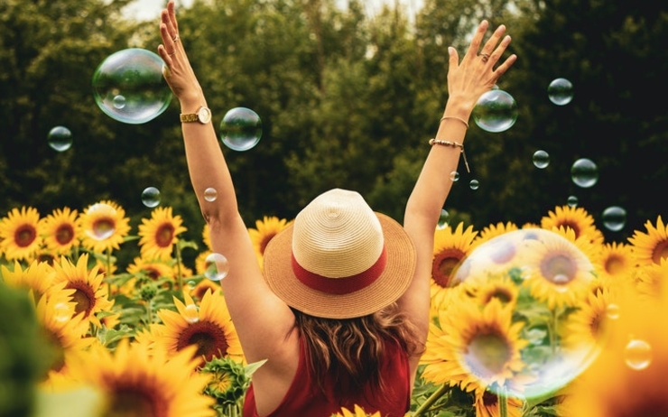Une femme lève les bras dans un champ de tournesol