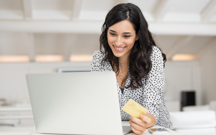 femme tenant une carte bancaire face ordinateur
