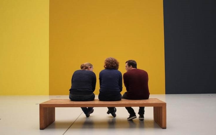 trois personnes assises dans un musée face à un murt jaune