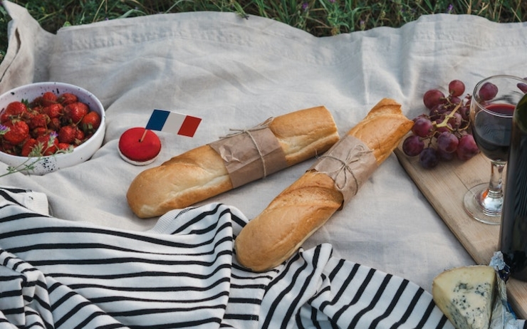Une baguette, un verre de vin, des fruits, du fromage et un drapeau français