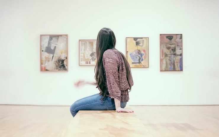 une fille assise observe les tableaux d'une exposition