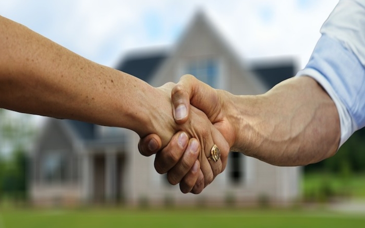 deux personnes se donnent la main pour accord devant une maison